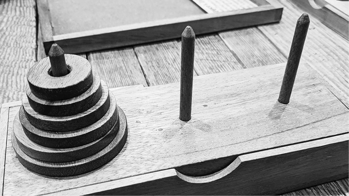 Picture of a wooden surface with three poles sticking out of it and a stack of disks, decreasing in size from bottom to top, placed on the first pole.